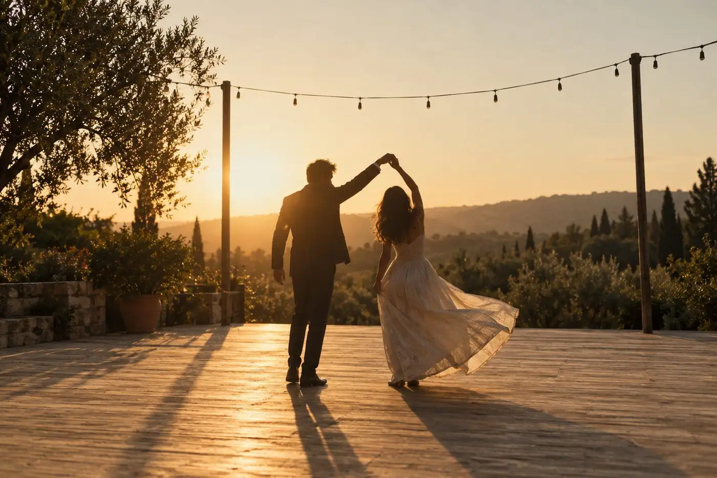 Una pareja bailando al atardecer bajo una guirnalda de luces, entre olivos